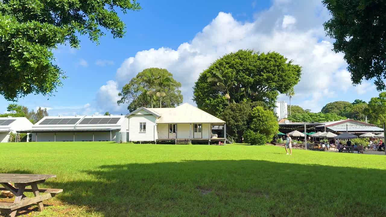 A serene farm scene with solar-paneled buildings, trees, and picnic tables under bright sunlight