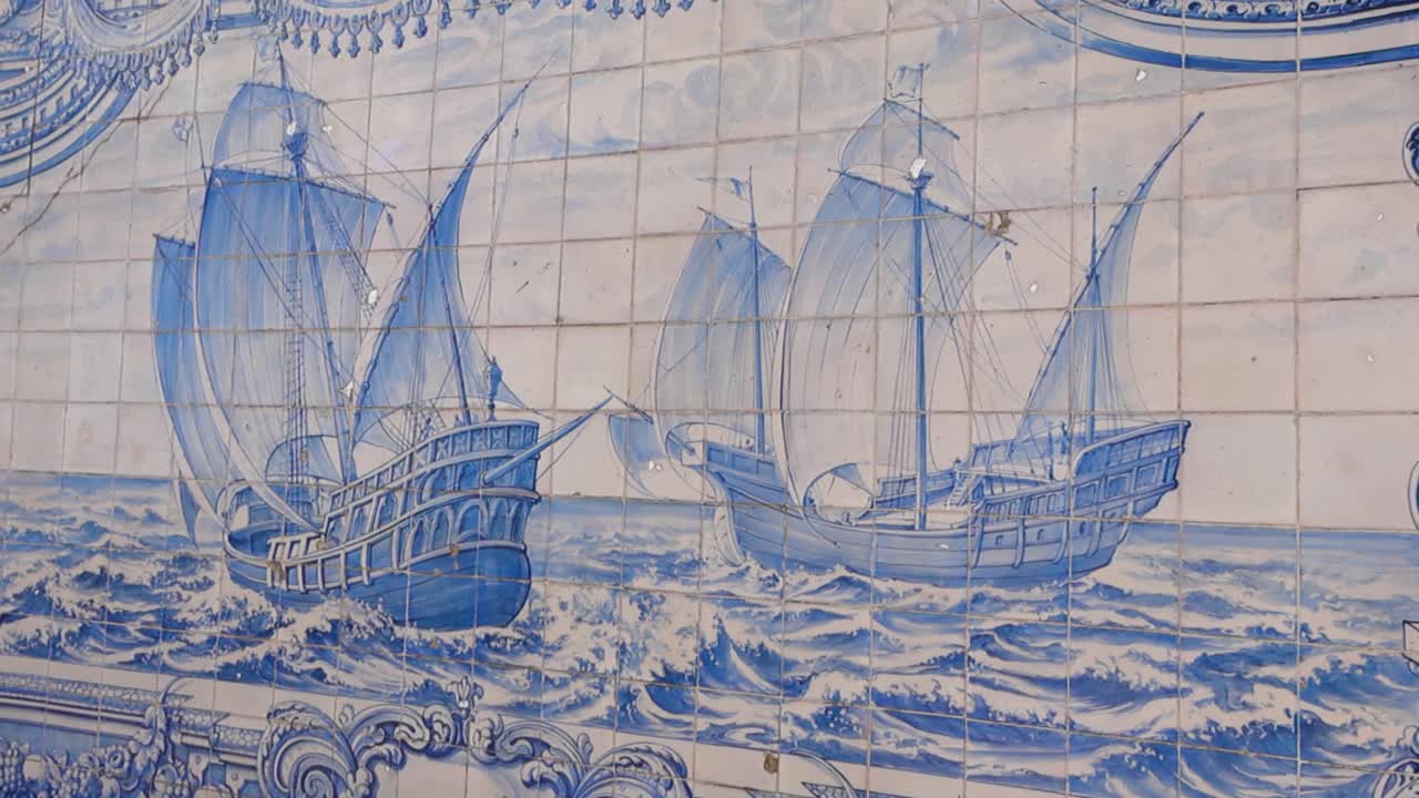 Il primo piano cinematografico rivela le tradizionali piastrelle di azulejos blu che illustrano navi a vela storiche in battaglia con le onde dell'oceano, mettendo in mostra il patrimonio marittimo portoghese e la maestria della ceramica decorativa alla luce del giorno