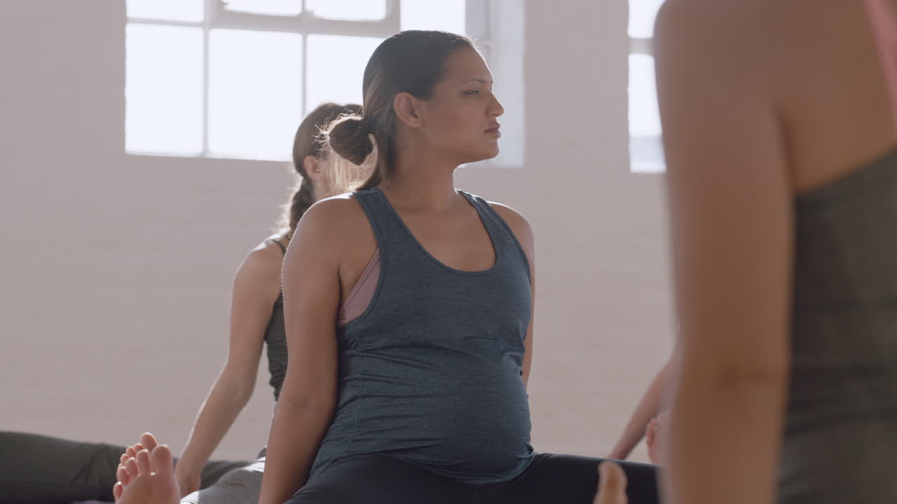 giovane donna incinta di razza mista in classe di yoga che esercita uno stile di vita sano praticando la meditazione respiratoria godendo di un allenamento di forma fisica fisica di gruppo all'alba