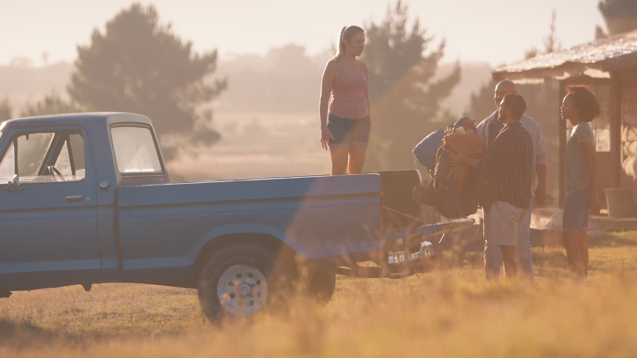 группа друзей загружает рюкзаки в пикап на дороге в каюту в сельской местности