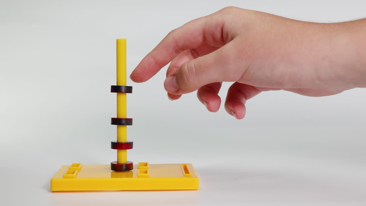 Hands manipulate magnetic rings on a yellow stand, illustrating magnetic forces in a well-lit, minimalistic setting