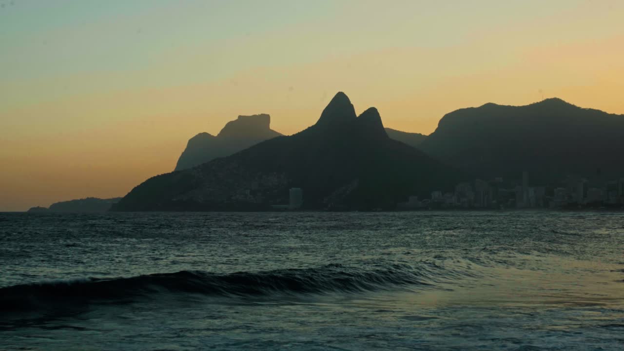Cinematic shot of the famous Two Brothers (Dois Irmãos) mountains silhouetted against a golden sky in Rio de Janeiro, Brazil