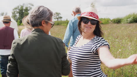 Rear-View-Of-Mature-Friends-Walking-Along-Path-Through-Yurt-Campsite