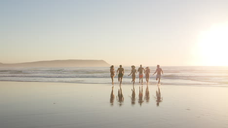 friends at sunset running along shore on beach vacation