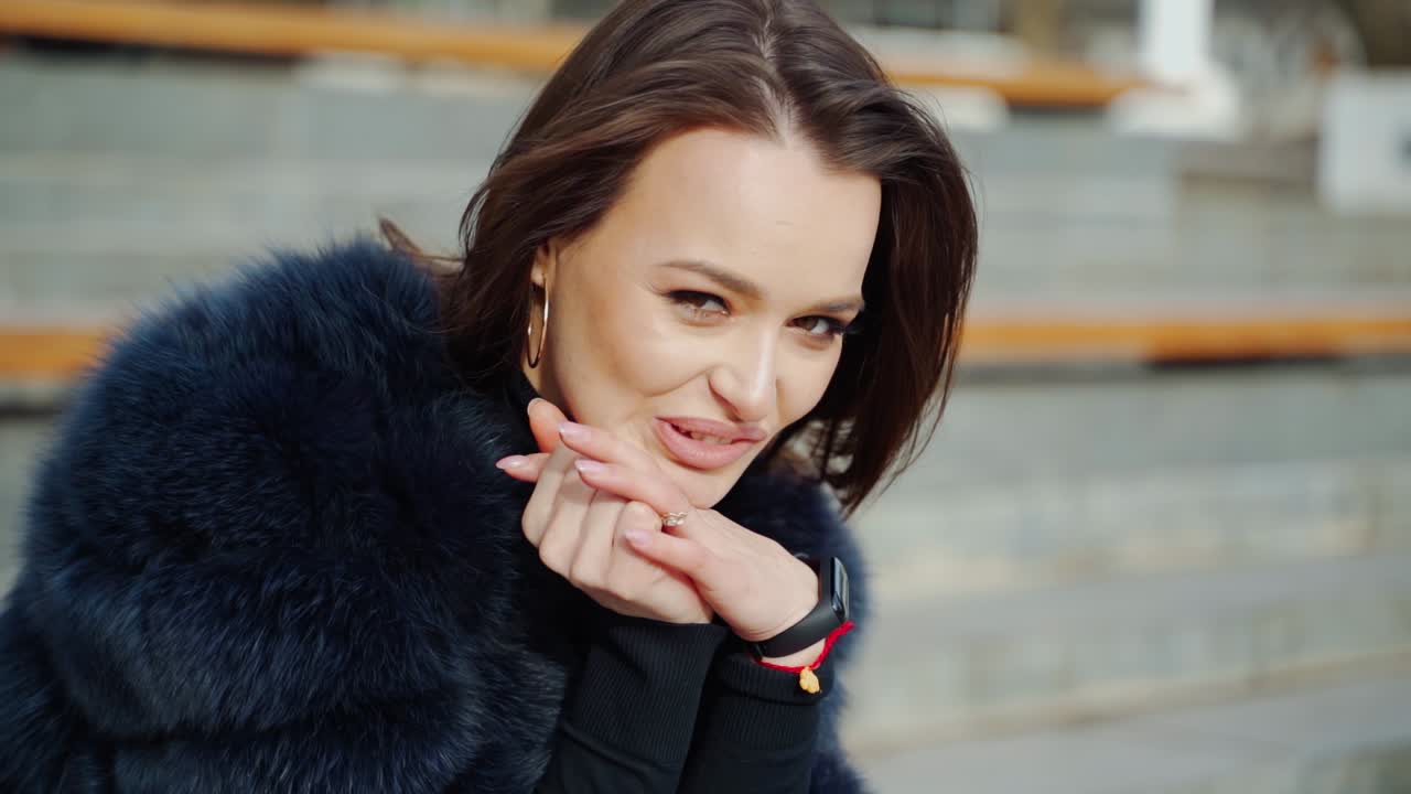 Portrait of attractive smiling brunette. Pretty face of a young woman in fur coat sitting outdoors and looking on camera. Close-up.