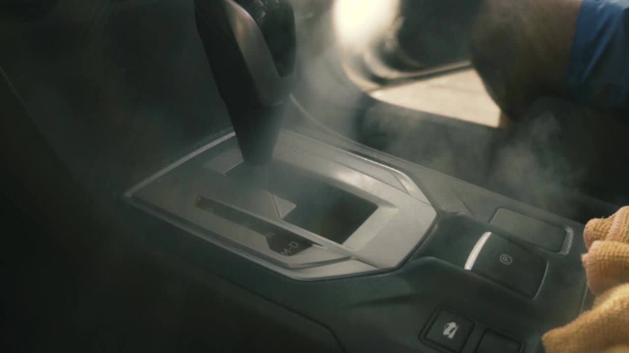 증기로 자동차 변속 레버 영역을 청소하는 검은 장갑을 끼고 있는 남성