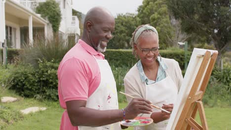 Feliz-Pareja-Afroamericana-Mayor-Pintando-Sobre-Caballete-De-Madera-En-El-Jardín,-Cámara-Lenta