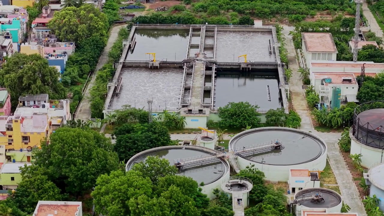 Aerial drone View of water treatment facility with circular tanks, filtration basins and processing structures surrounded by buildings and trees in Chennai Tamil Nadu India