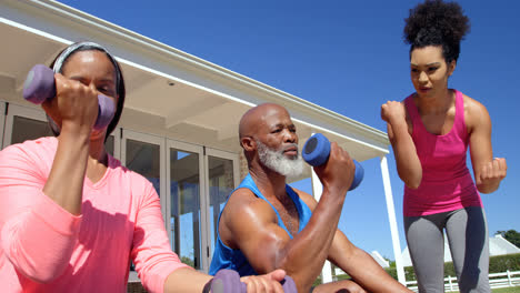 Low-angle-view-of-mixed-race-female-trainer-exercising-with-mature-black-couple-in-backyard-4k