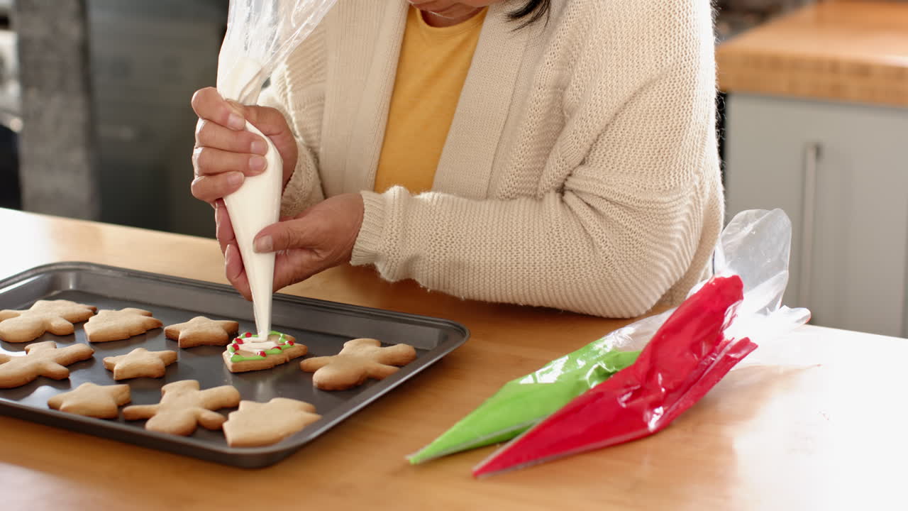 Decorating Christmas cookies at home, senior woman using icing with care