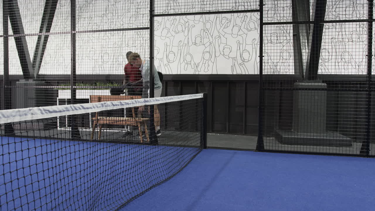 Two diverse men preparing for padel tennis match on indoor court, holding rackets
