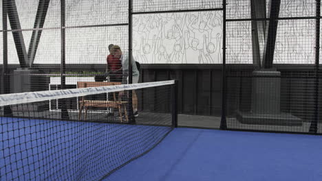 two diverse men preparing for padel tennis match on indoor court, holding rackets