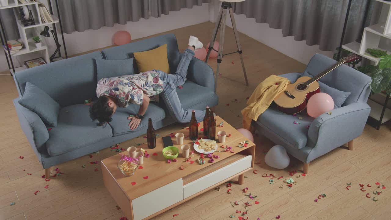 vista superior de un hombre asiático borracho se despierta después de dormir en un sofá en la sala de fiestas en casa