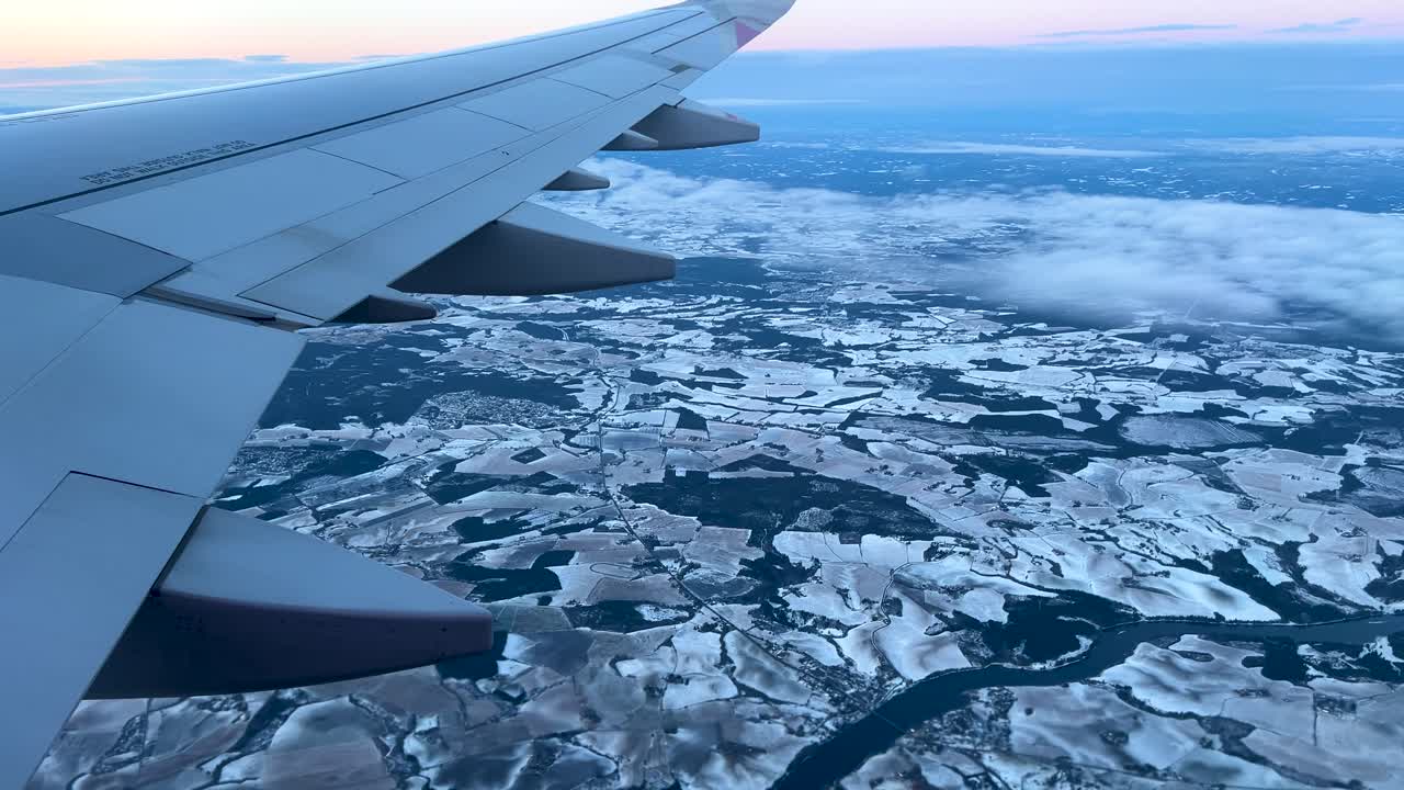 Flying over snowy European landscape at dusk, POV view from side of airplane
