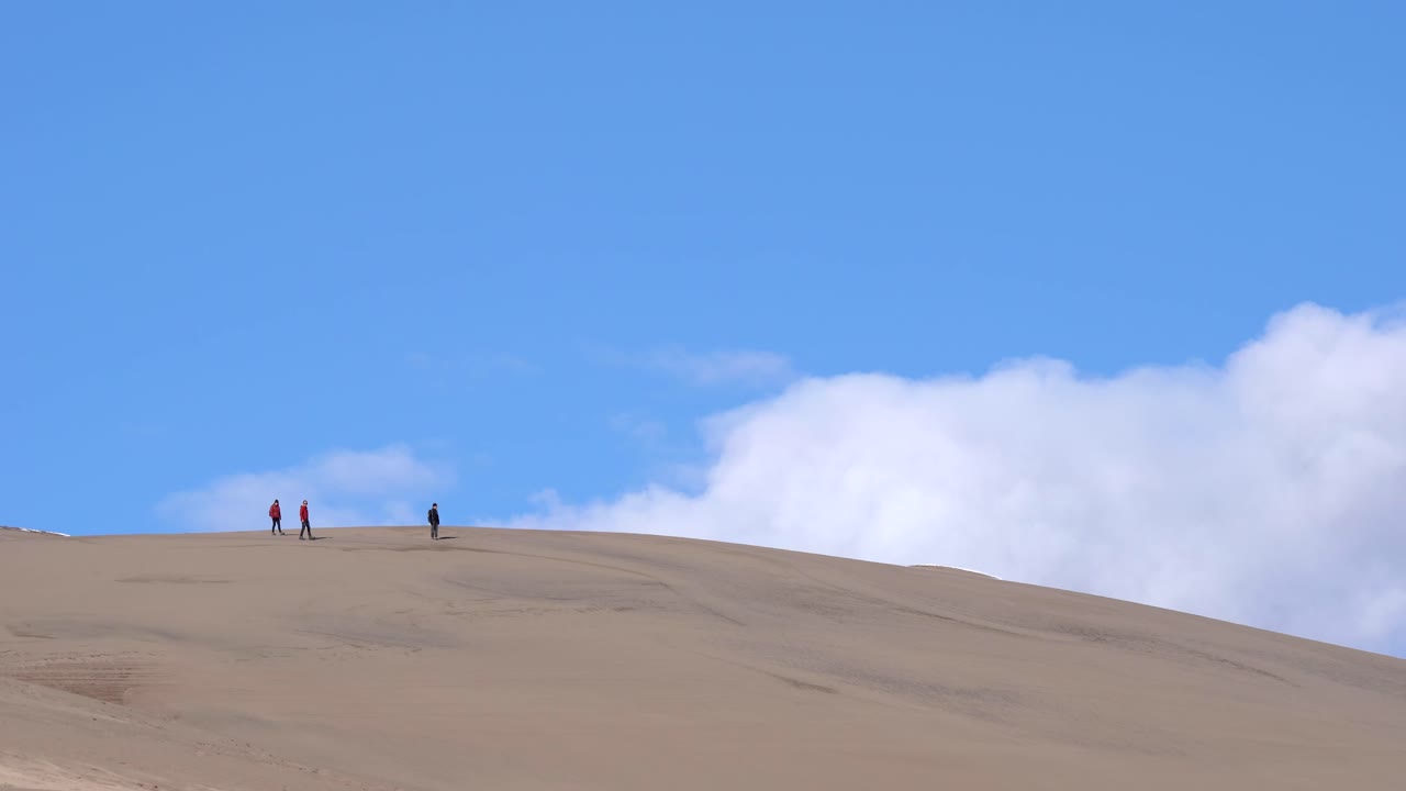 화창한 날 모래 언덕 위로 하이킹을 하는 사람들
