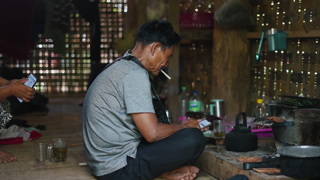 Man sitting indoors smoking and using a cell phone