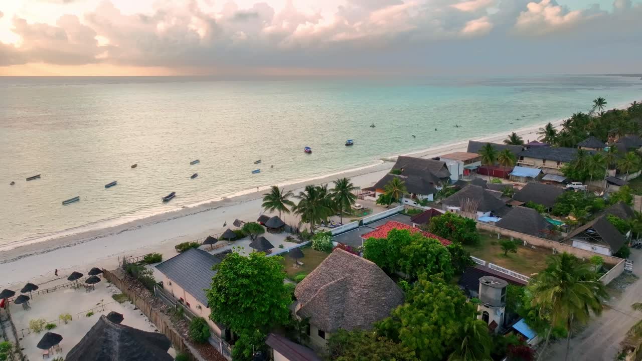 Drone rises from the ocean to capture Paje, Zanzibar: golden sunset illuminates beach and cityscape