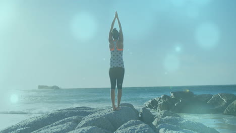 animación de puntos de luz sobre mujer biracial practicando yoga en la playa