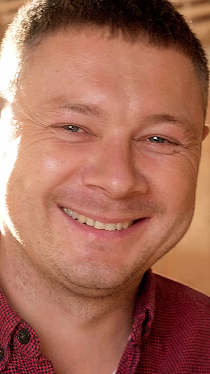Smiling man with short hair wearing a red checkered shirt in a warm indoor setting