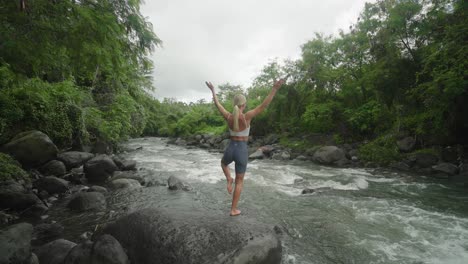 mujer joven haciendo pose de árbol de yoga, río tropical en indonesia, slowmo