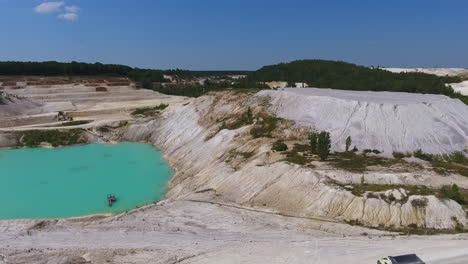 hilly and sloping area of a kaolin quarry producing raw kaolin. little blue lake reflecting the sky. green forest backdrop.