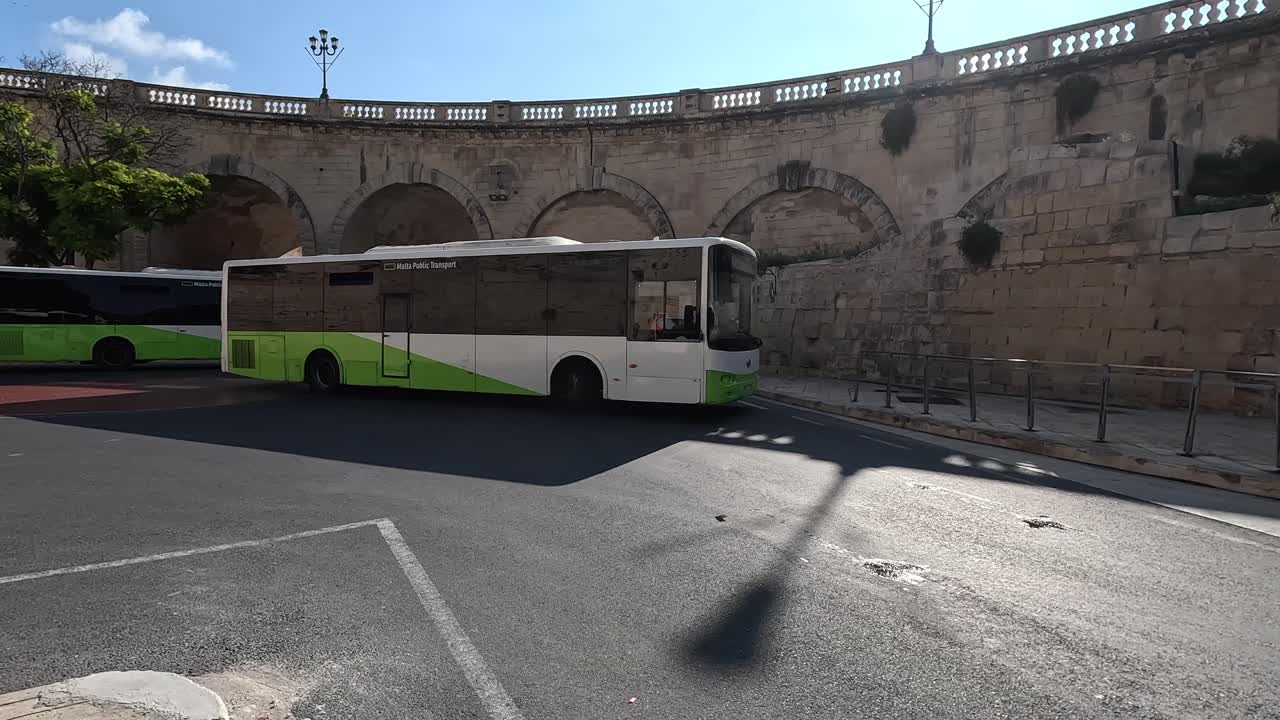 A white and green Malta Public Transport bus on an urban street