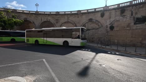 a white and green malta public transport bus on an urban street