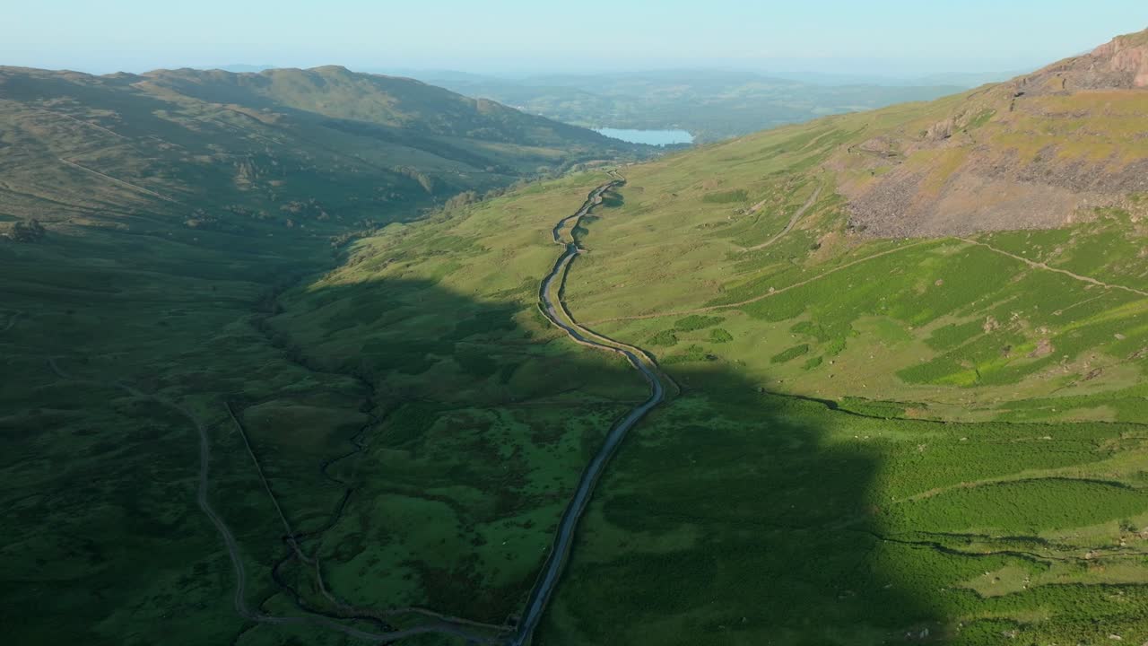 Mountain pass road snaking across mountainside at sunrise. Summer. Kirkstone Pass, Lake District, Cumbria, UK