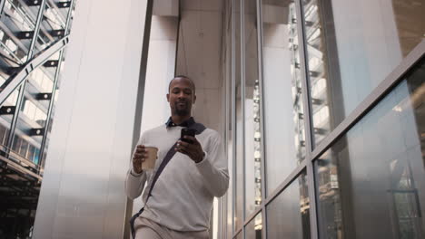 african american businessman walking through city using smart phone