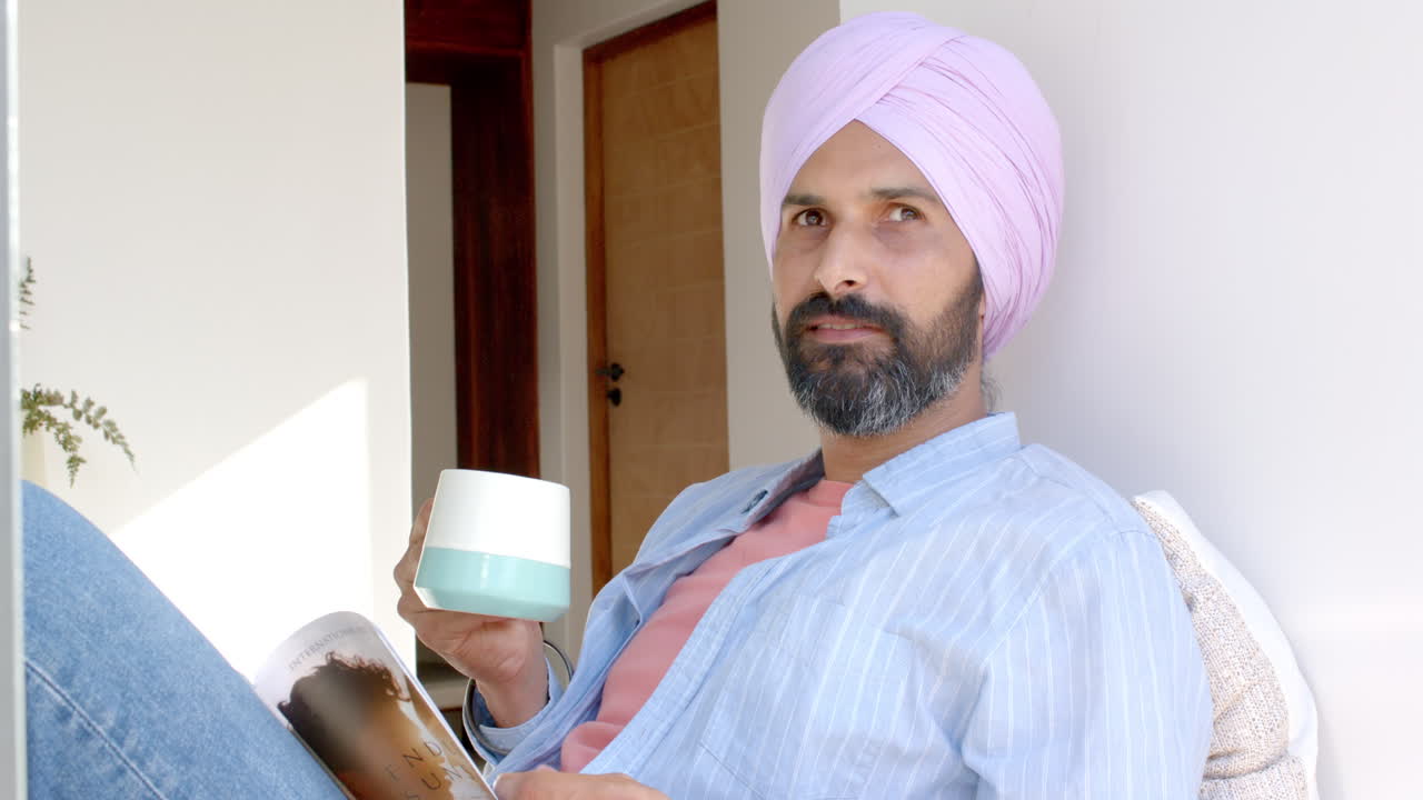 Relaxing at home, man in turban holding coffee cup and reading magazine