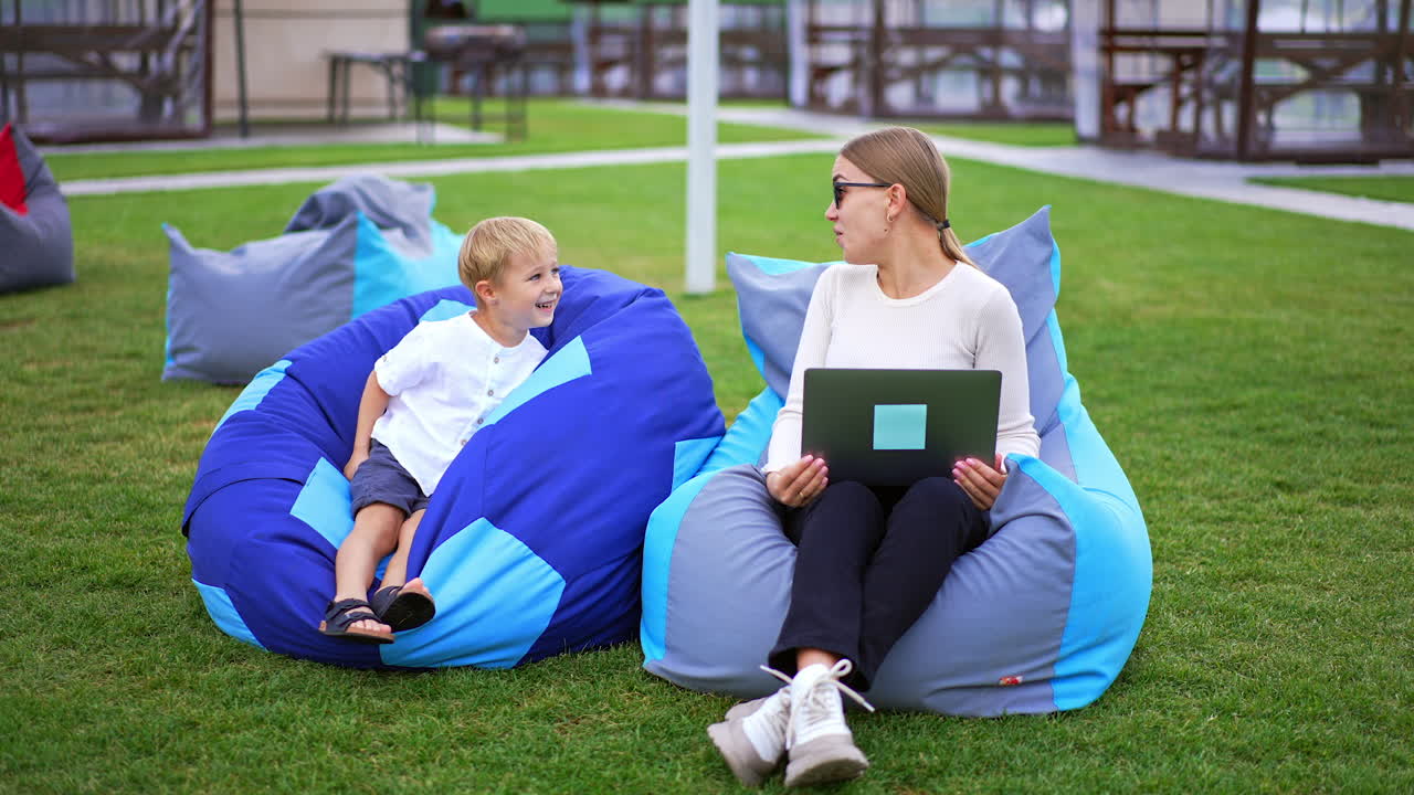Pleasant time spending outdoors in the resort area. Woman showing something on laptop to a boy sitting next.