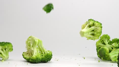 broccoli pieces falling and bouncing in slow motion onto white studio backdrop in 4k