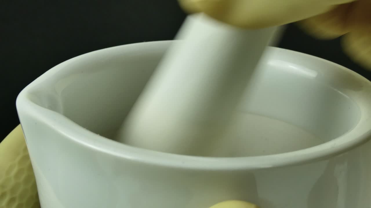 장갑을 쓴 손은 포셀린 모터로 정확하게 작업하며, 통제된 실험실 환경에서 의약품 공식의 복합을 보여줍니다. 이 장면은 과학적 엄격성을 강조합니다.