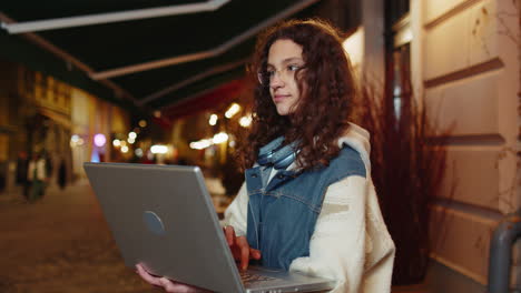 happy girl working online distant job with laptop in city street browsing website chatting