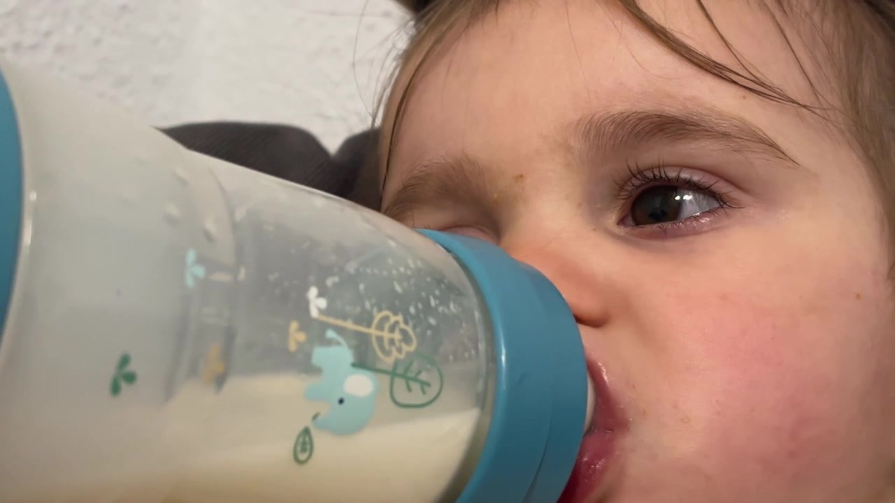 Primo piano di un bambino piccolo che beve latte dal biberon al chiuso, scena rilassata e tranquilla.