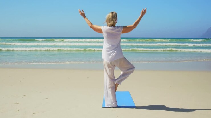 Vista posteriore di donna anziana caucasica attiva che pratica yoga sulla spiaggia 4k