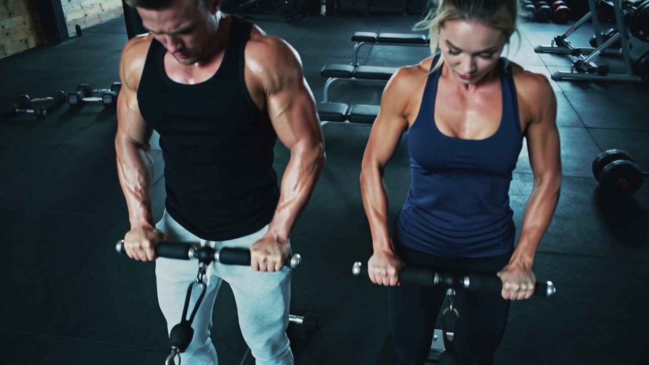 Afferrando la barra, partner di allenamento in forma eseguono rematore ai cavi in palestra per la forza, indossando canotte.