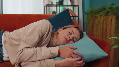 tired young woman lying down in bed taking a rest at home, napping, falling asleep on orange couch