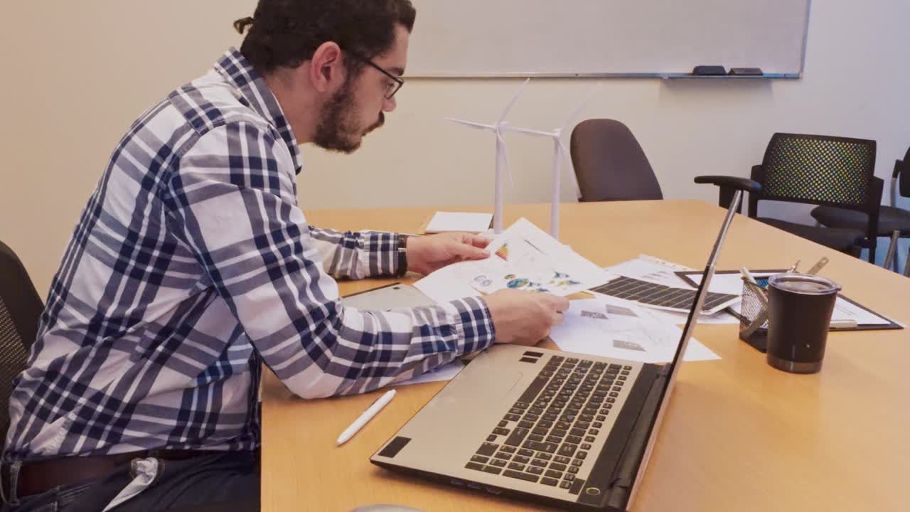 Man working at a desk with models of wind turbines and solar panels