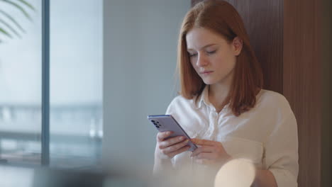 young woman working in office is using mobile phone for surfing internet and social media during work day