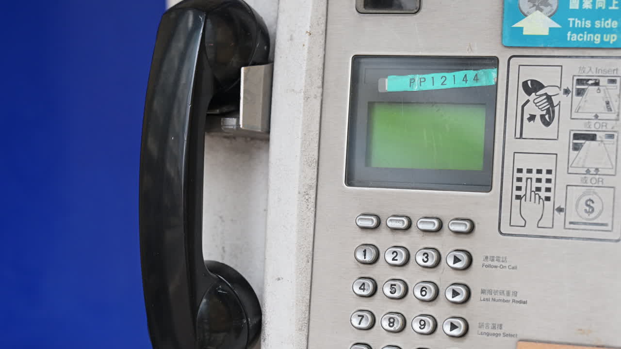 Detailed view of a working public telephone booth with a receiver and keypad. Visual representation of active legacy technology and the survival of traditional telecommunications in a high-tech city