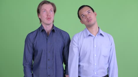 two businessman looking bored and stressed against green studio background