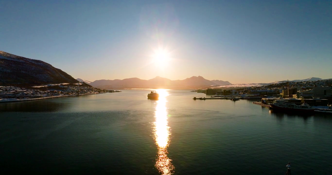 Barco costero Hurtigruten navegando hacia el puerto de Tromso para atracar, vista aérea al atardecer.