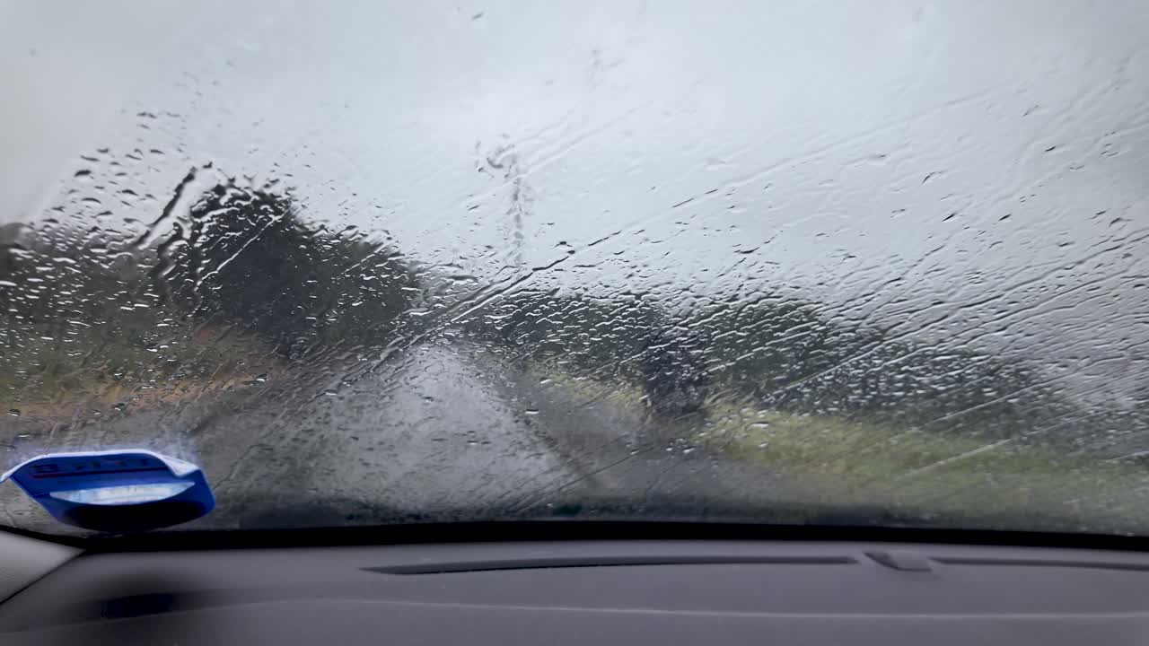 Raindrops covering a car windshield, limiting visibility of the road and gloomy sky