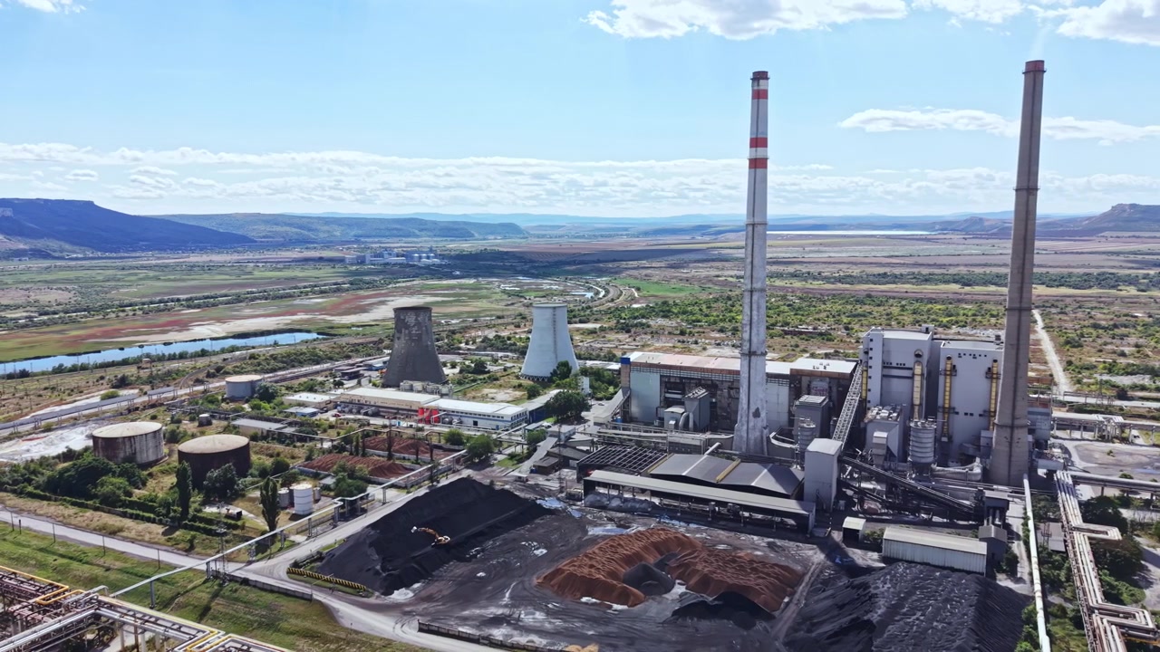 Centrale a carbone situata vicino a un fiume con grandi torri di raffreddamento e ciminiere sotto un cielo sereno