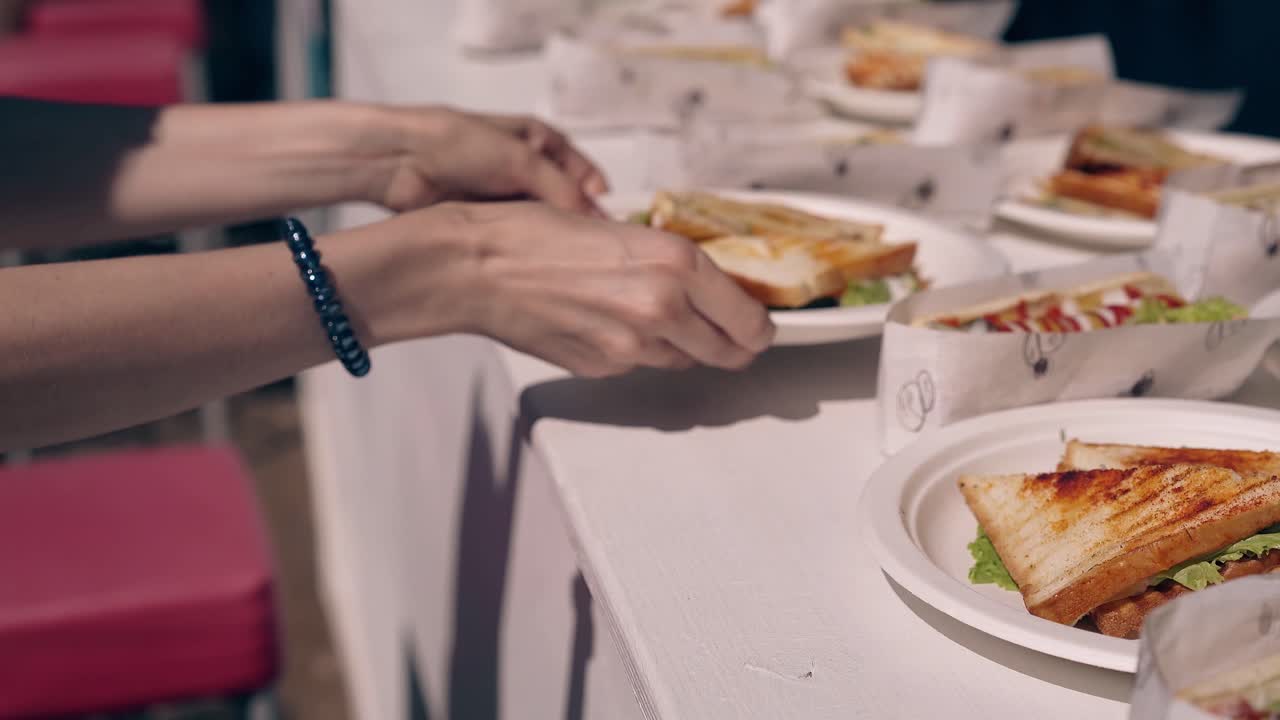 여름에 해변에 있는 소녀들은 테이블에서 샌드위치를 가져갑니다.