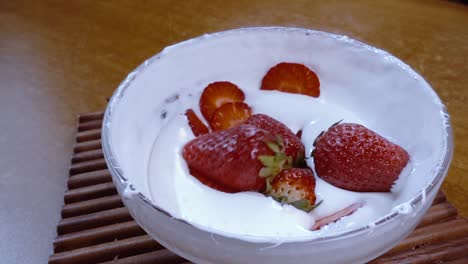 fresas cayendo en un tazón de crema batida en cámara lenta con disparo de seguimiento de rotación.