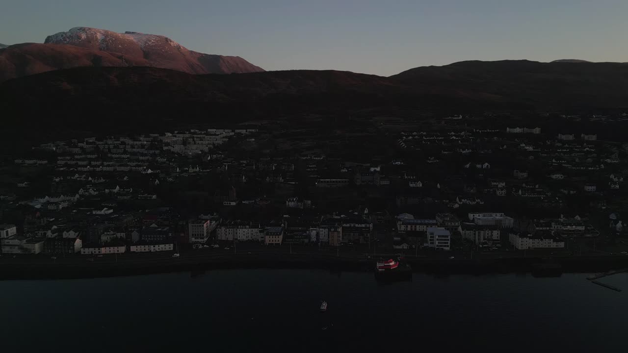 Vista aerea di Fort William, in Scozia, con Ben Nevis sullo sfondo, splendidamente illuminato dalla luce del tramonto in una limpida giornata invernale. Drone che vola all'indietro