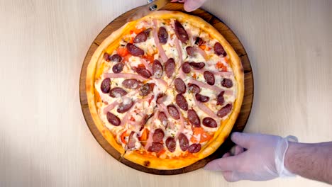 el cocinero corta pizza con salchichas ahumadas, jamón y queso.
