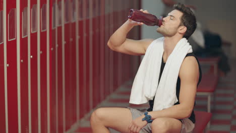 un deportista cansado bebiendo agua en el vestuario.
